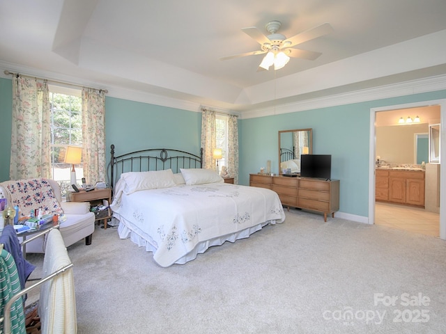 bedroom featuring a tray ceiling, crown molding, light colored carpet, ensuite bathroom, and baseboards