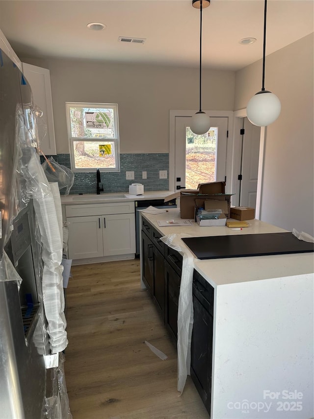 kitchen featuring tasteful backsplash, light wood-style flooring, a kitchen island, pendant lighting, and a sink