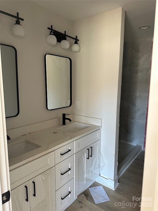 full bath featuring a stall shower, wood finished floors, a sink, and double vanity