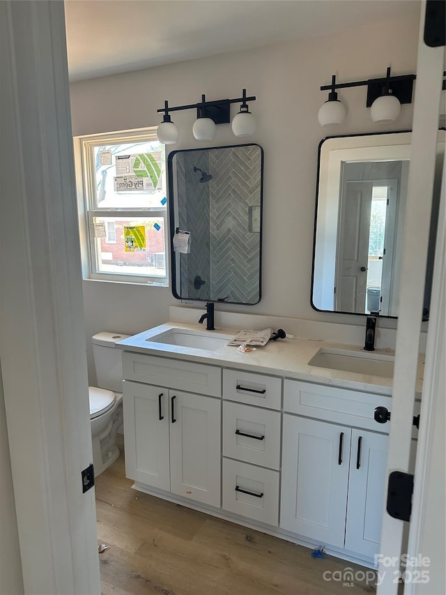 full bath with a shower stall, toilet, double vanity, wood finished floors, and a sink