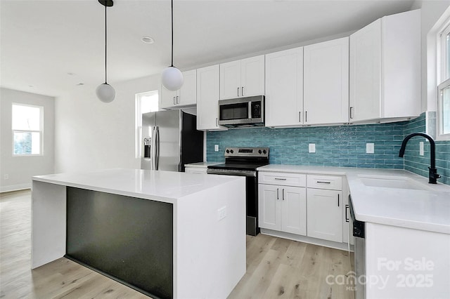 kitchen featuring light wood finished floors, a kitchen island, decorative backsplash, appliances with stainless steel finishes, and a sink