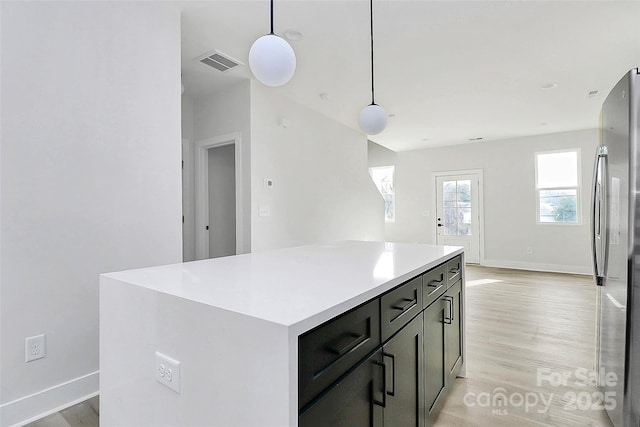 kitchen with visible vents, a kitchen island, freestanding refrigerator, light wood finished floors, and light countertops