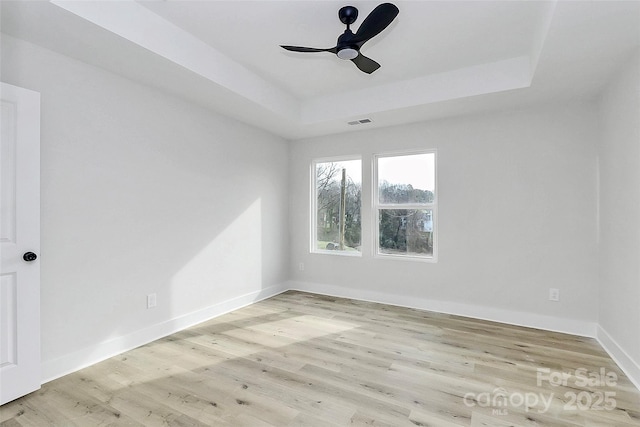 unfurnished room with visible vents, a tray ceiling, wood finished floors, baseboards, and ceiling fan