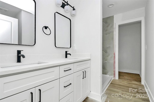 bathroom with visible vents, double vanity, a tile shower, wood finished floors, and a sink