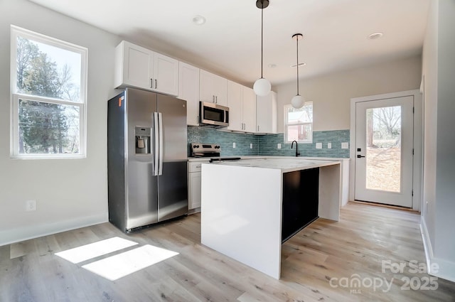 kitchen featuring decorative backsplash, white cabinets, appliances with stainless steel finishes, a sink, and a center island