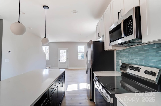 kitchen with light countertops, stainless steel appliances, backsplash, light wood-style floors, and pendant lighting