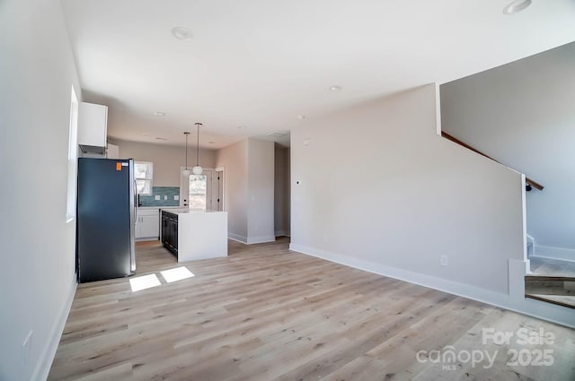 unfurnished living room featuring stairs, light wood-style floors, and baseboards