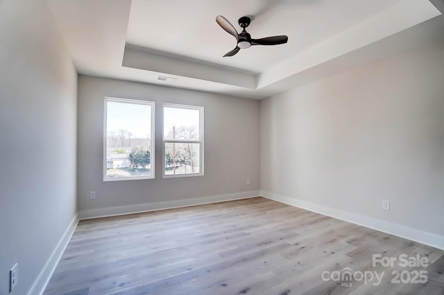 spare room featuring baseboards, a tray ceiling, and light wood-type flooring