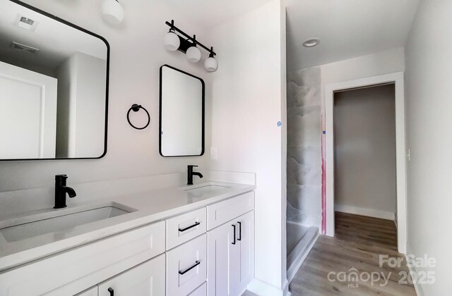 full bathroom with double vanity, a sink, a tile shower, and wood finished floors