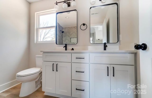 bathroom with visible vents, double vanity, toilet, wood finished floors, and a sink