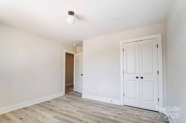 unfurnished bedroom featuring baseboards, light wood-style flooring, and a closet