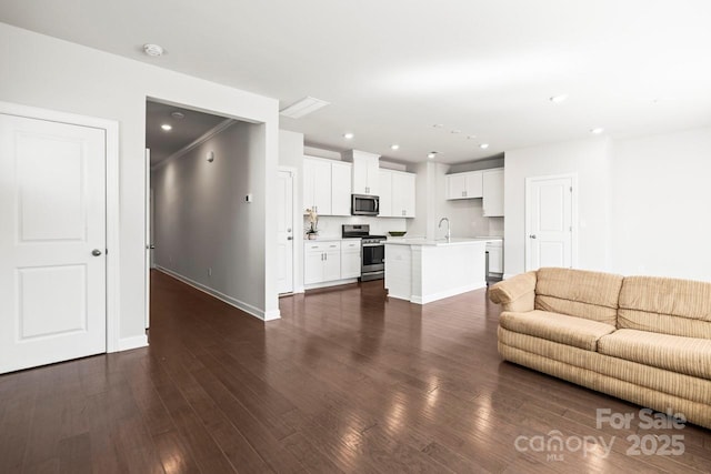 unfurnished living room featuring dark wood-style floors, baseboards, a sink, and recessed lighting