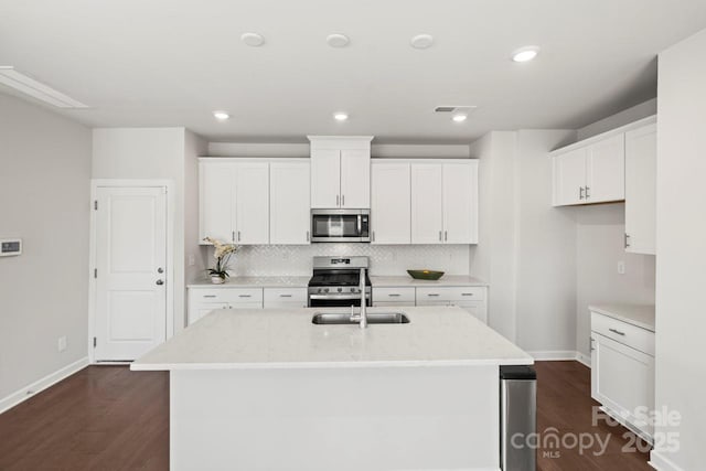 kitchen with dark wood-style floors, a kitchen island with sink, stainless steel appliances, white cabinetry, and backsplash