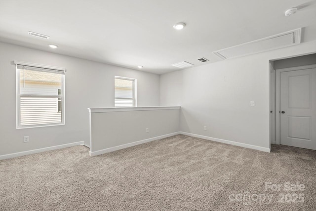 carpeted empty room featuring attic access, visible vents, and baseboards