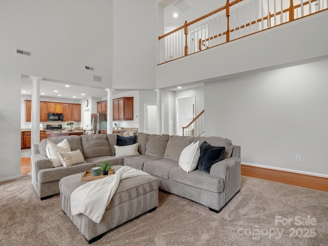 living area featuring baseboards, visible vents, ornate columns, and a towering ceiling