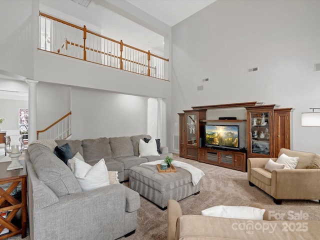 carpeted living area featuring ornate columns, a high ceiling, and visible vents