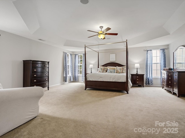 bedroom with visible vents, light carpet, baseboards, a tray ceiling, and a ceiling fan