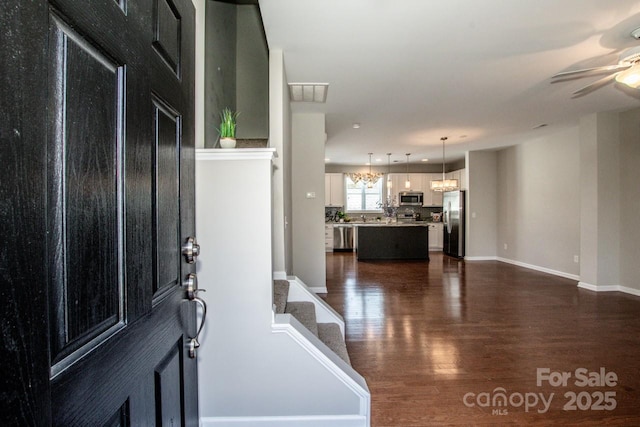 foyer featuring baseboards, visible vents, dark wood finished floors, and ceiling fan with notable chandelier