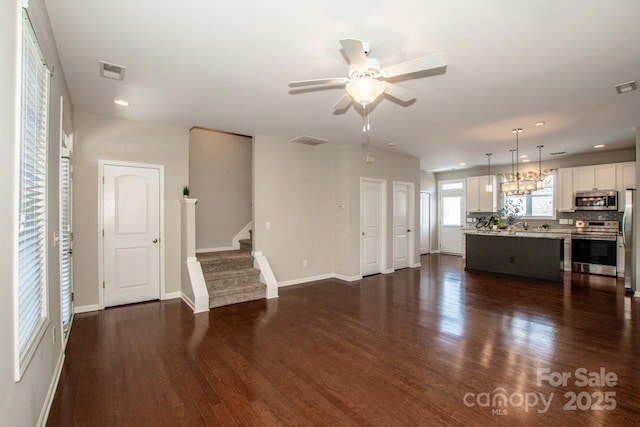 unfurnished living room with dark wood finished floors, visible vents, ceiling fan, baseboards, and stairs