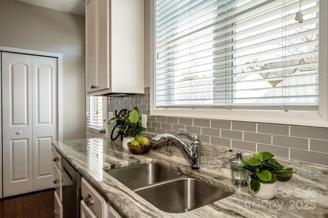 kitchen featuring stainless steel dishwasher, light stone counters, backsplash, and a sink