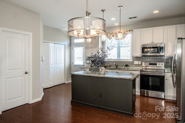 kitchen featuring light stone counters, a center island, visible vents, appliances with stainless steel finishes, and decorative backsplash