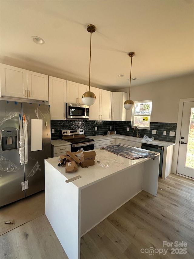 kitchen with light wood-type flooring, appliances with stainless steel finishes, white cabinets, and a center island