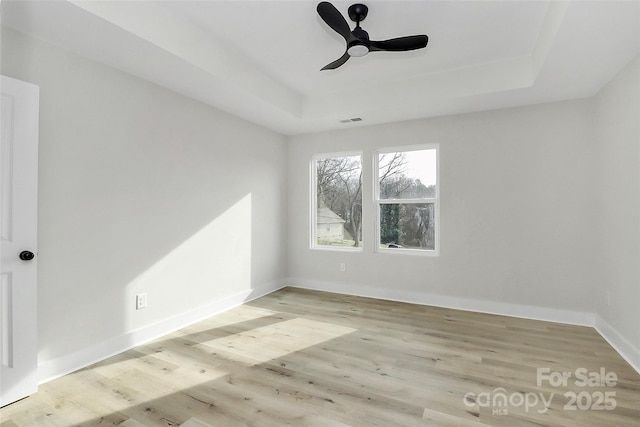 unfurnished room featuring ceiling fan, a tray ceiling, visible vents, and wood finished floors