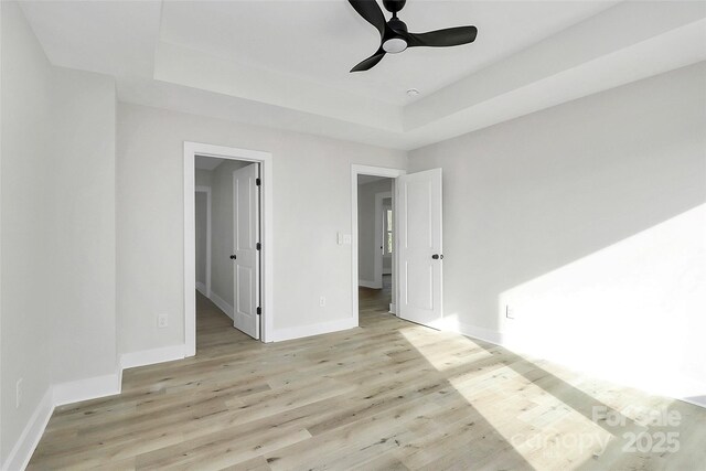 empty room featuring baseboards, a ceiling fan, light wood-type flooring, and a tray ceiling