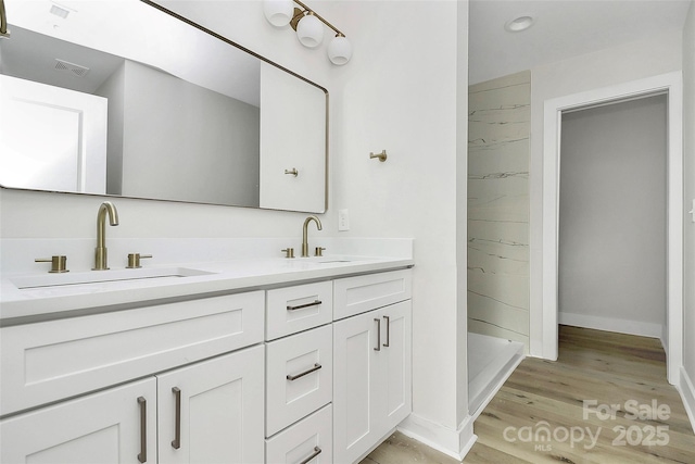 bathroom featuring visible vents, a sink, wood finished floors, a shower stall, and double vanity