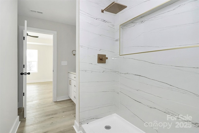 full bath featuring a marble finish shower, visible vents, baseboards, and wood finished floors