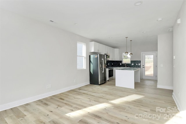 kitchen featuring light wood finished floors, a center island, decorative backsplash, stainless steel appliances, and white cabinetry