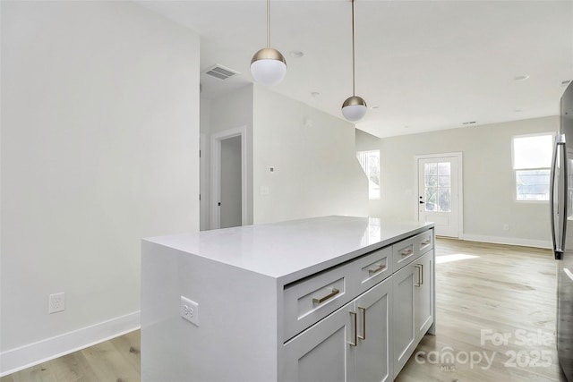 kitchen featuring visible vents, light wood finished floors, pendant lighting, light countertops, and baseboards