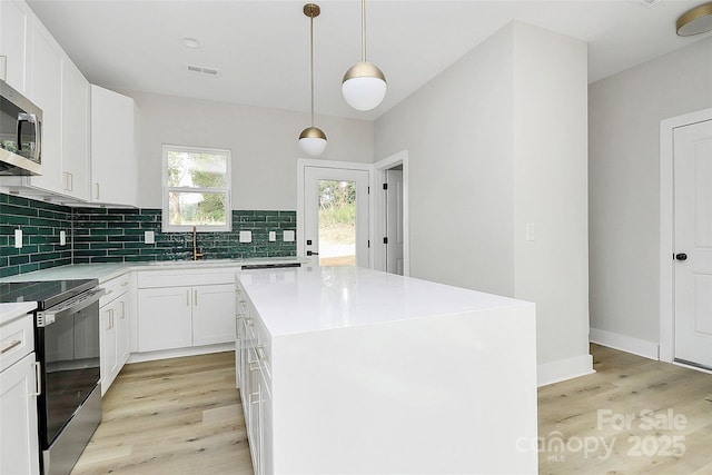 kitchen featuring visible vents, stainless steel appliances, light countertops, light wood-type flooring, and backsplash