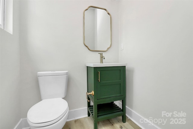 bathroom with vanity, toilet, wood finished floors, and baseboards