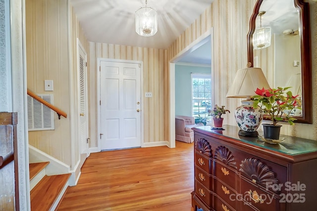 foyer featuring light wood finished floors, wallpapered walls, baseboards, stairs, and ornamental molding