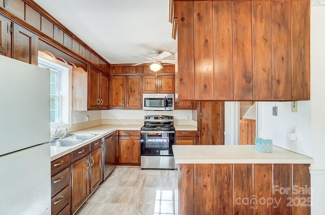 kitchen with a peninsula, ceiling fan, a sink, light countertops, and appliances with stainless steel finishes