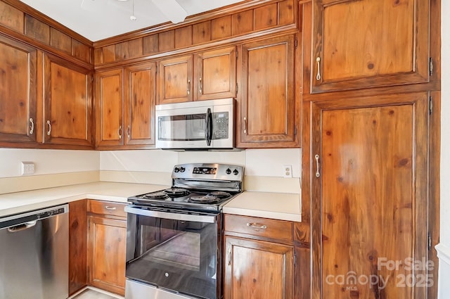 kitchen featuring stainless steel appliances, brown cabinetry, and light countertops