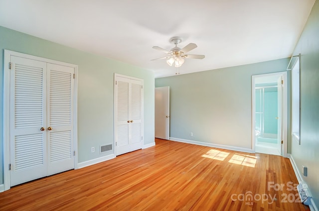 unfurnished bedroom featuring visible vents, baseboards, light wood-type flooring, and multiple closets