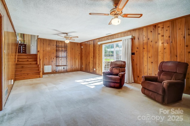 sitting room with stairs, visible vents, ceiling fan, and carpet flooring