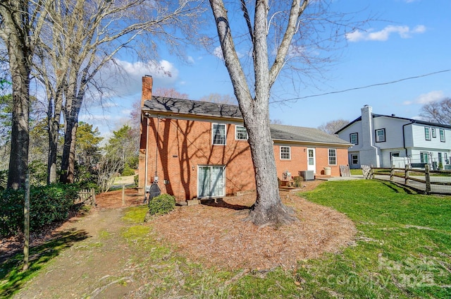 rear view of property featuring brick siding, central air condition unit, a lawn, and a chimney