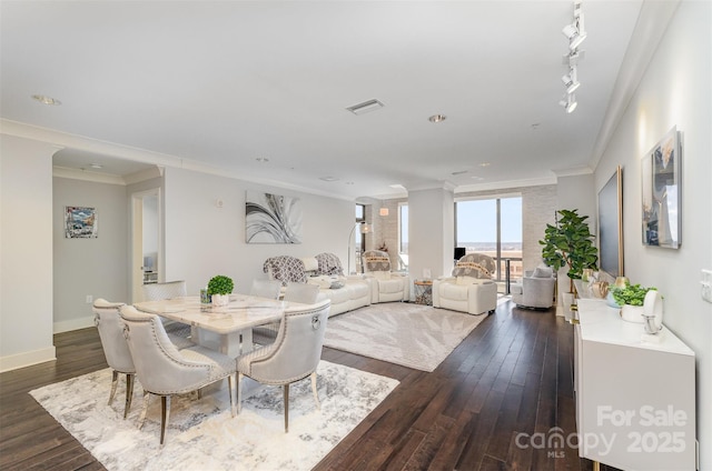 dining space featuring baseboards, visible vents, dark wood finished floors, rail lighting, and crown molding