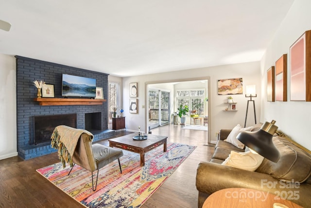 living room featuring a brick fireplace, baseboards, and wood finished floors