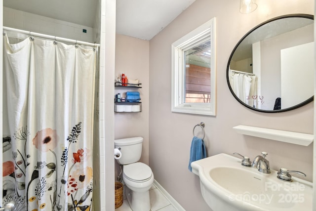 bathroom featuring curtained shower, toilet, a sink, baseboards, and tile patterned floors