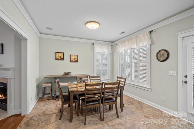 dining room with baseboards, a premium fireplace, visible vents, and crown molding