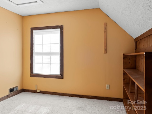 interior space featuring baseboards, visible vents, vaulted ceiling, a textured ceiling, and carpet floors