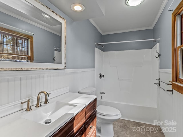 bathroom featuring toilet, vanity, ornamental molding, wainscoting, and tub / shower combination