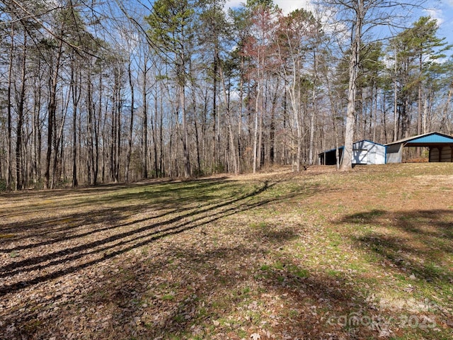 view of yard with a detached carport, a wooded view, and an outbuilding