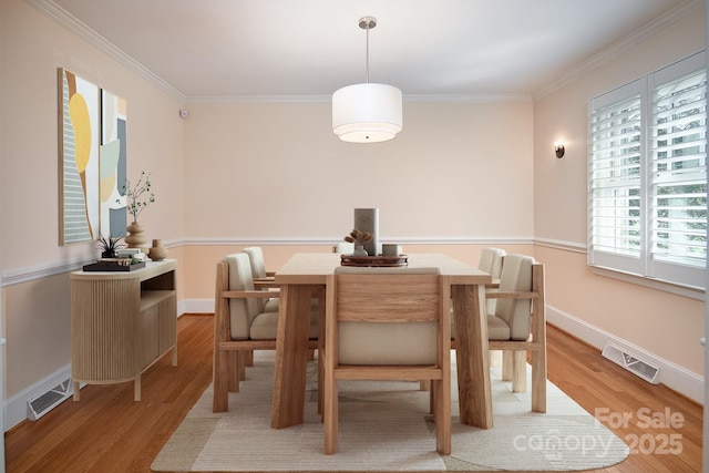 dining space featuring baseboards, wood finished floors, visible vents, and ornamental molding