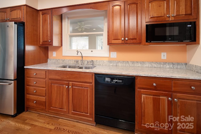 kitchen featuring black appliances, brown cabinetry, light wood-style floors, and a sink