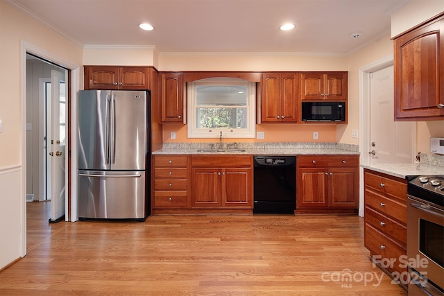 kitchen with brown cabinetry, black appliances, light wood-type flooring, and a sink